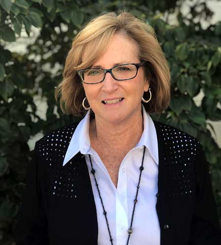 Mrs. Sargent. She has blonde hair and glasses with a black frame, wearing a white button up shirt and a black cardigan.